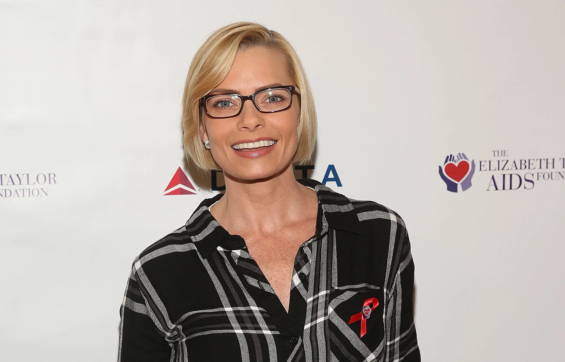 Blonde woman in glasses and plaid shirt at The Elizabeth Taylor AIDS Foundation event, smiling.
