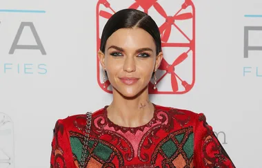Young woman with short dark hair, wearing a colorful patterned dress, standing in front of a logo backdrop.