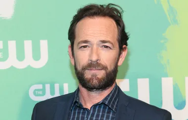 A man with short hair and a beard in a suit at a CW event, standing against a green background.