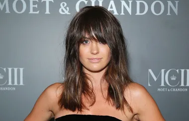 Young woman with long dark hair and bangs in a black strapless outfit, posing at a Moët & Chandon event backdrop.
