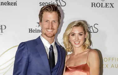 Two people posing together at an event, smiling, with branded background logos.