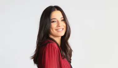 A smiling woman with long dark hair wearing a red blouse against a light background.