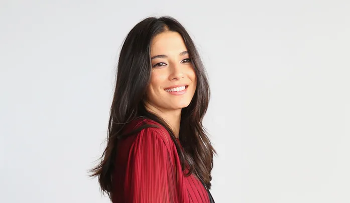A smiling woman with long dark hair wearing a red blouse against a light background.