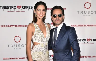 Two people pose together at the Maestro Cares Foundation event; one in a patterned dress, the other in a blue suit and sunglasses.