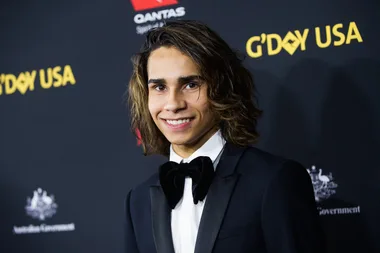 Young man in a tuxedo smiling at an event with "G'DAY USA" in the background.