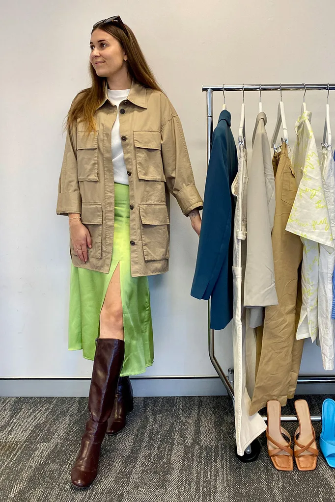 a-woman-wears-brown-cargo-over-coat-with-white-tee-green-skirt-brown-knee-high-boots