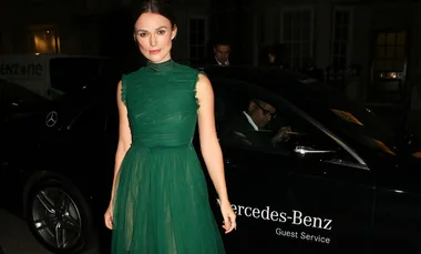 A person in a green dress stands next to a black Mercedes-Benz car at night.