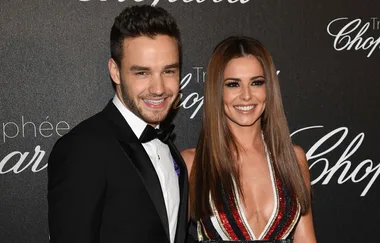Two people smiling on a red carpet event, with branded backdrop.