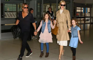 Family walking through an airport terminal, with parents holding hands with two young children.