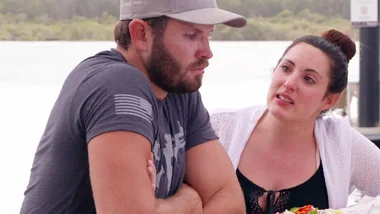 Two people at an outdoor location having a serious conversation by the water.