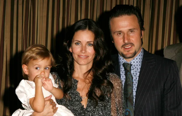 Family portrait with a woman holding a toddler and a man standing beside them, all smiling.