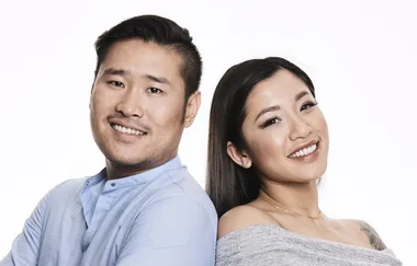 Two people smiling, standing back-to-back against a white background.