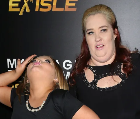 Two people posing, one looking upwards with hand on head, the other smiling, in front of a black backdrop.