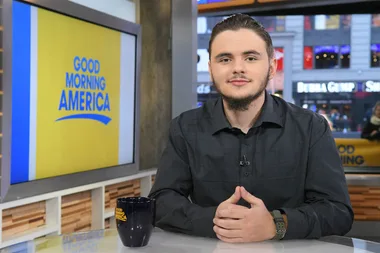 A person sitting at a "Good Morning America" interview desk, with the show's logo displayed in the background.