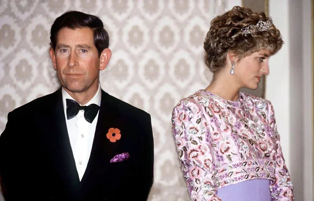 Prince Charles in a tuxedo and Princess Diana in a pink dress, standing back to back at an event.