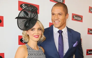 A woman in a black hat and dress stands beside a smiling man in a suit at a Swisse event backdrop.