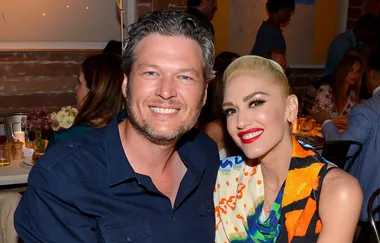 A smiling man and woman pose closely together at a lively indoor event, surrounded by other seated guests.