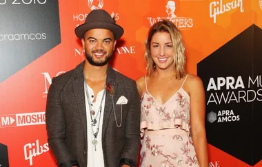 Two people smiling at the APRA Music Awards, standing in front of an orange and black backdrop.