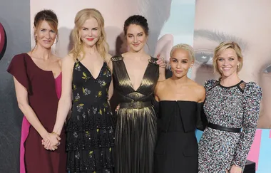 Five women in elegant dresses pose together at an event, smiling.