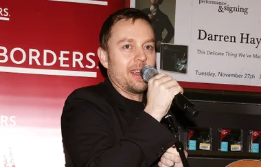 Singer at a Borders event holding a microphone, with a poster for a Darren Hayes performance and signing in the background.