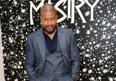 Man in a gray suit and navy shirt stands smiling in front of a black and white patterned wall with text "MASRY."