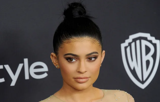 Person with dark hair in a bun, posing at a formal event with a neutral expression, wearing a beaded outfit.