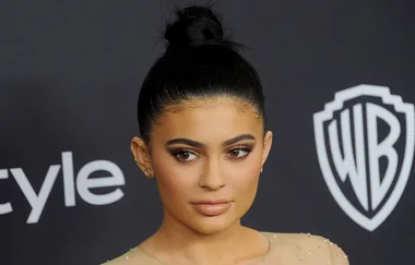 Person with dark hair in a bun, posing at a formal event with a neutral expression, wearing a beaded outfit.