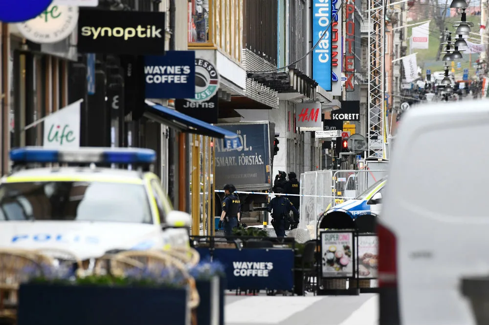 Street scene in Stockholm with police presence and various shop signs visible, including Wayne's Coffee and H&M.