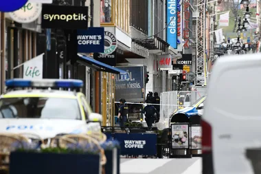 Street scene in Stockholm with police presence and various shop signs visible, including Wayne's Coffee and H&M.