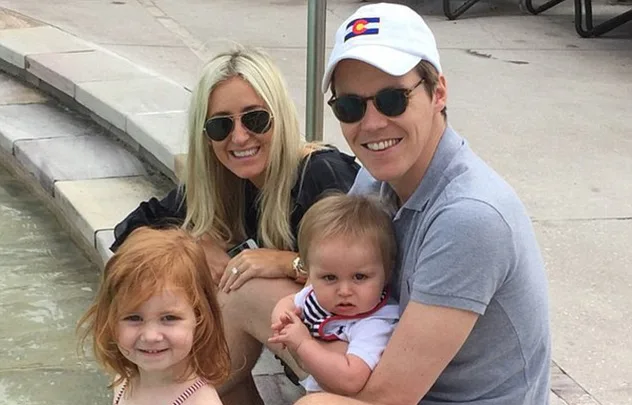 A family with two adults and two children sitting by a pool, all smiling.