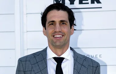 A man in a gray checkered suit and black tie, smiling against a white background.