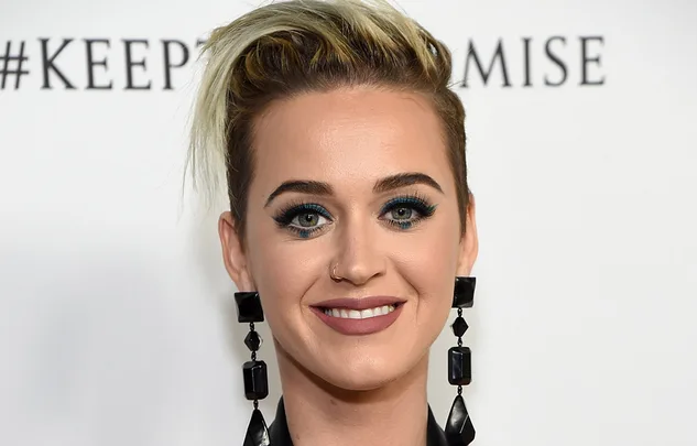 Woman with short blonde hair, large black earrings, and a nose ring, smiling against a white backdrop with text.