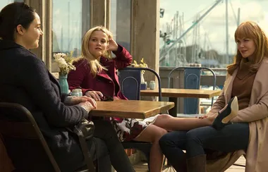 Three women sitting at an outdoor café table, laughing and chatting on a sunny day.