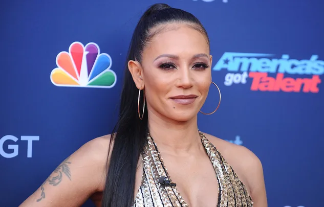 A woman with a long ponytail and hoop earrings attends "America's Got Talent" event, with logos in the background.