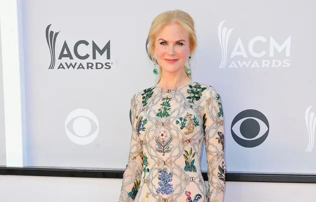 A person in a floral dress stands smiling at the ACM Awards with logos in the background.