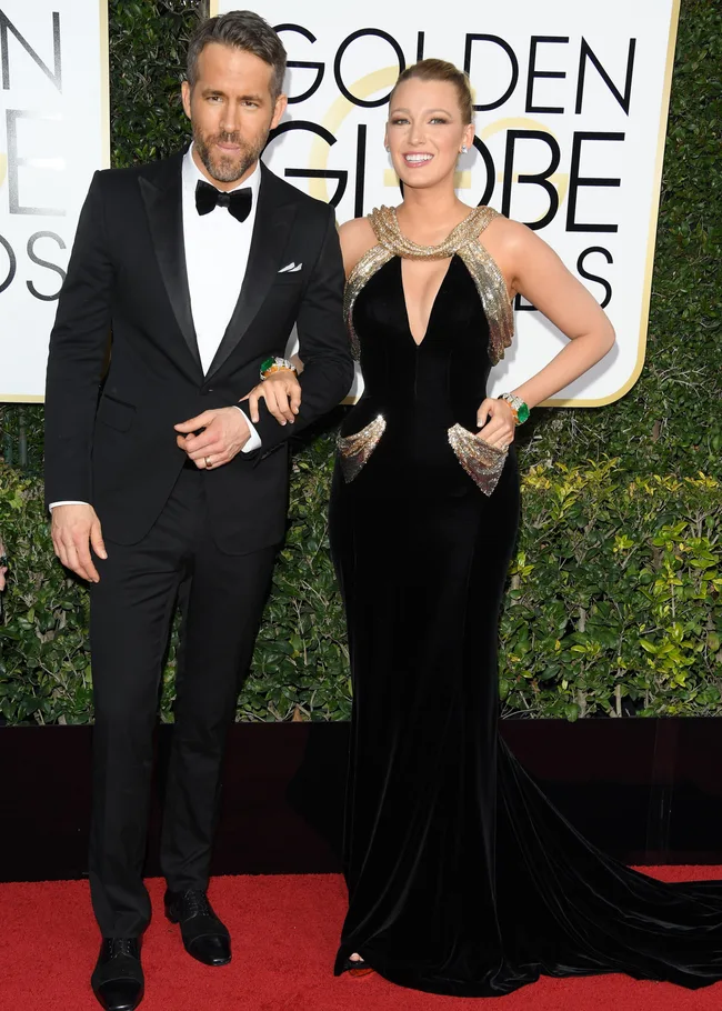 "Man in black tuxedo and woman in black gown with gold accents on red carpet at Golden Globe Awards."