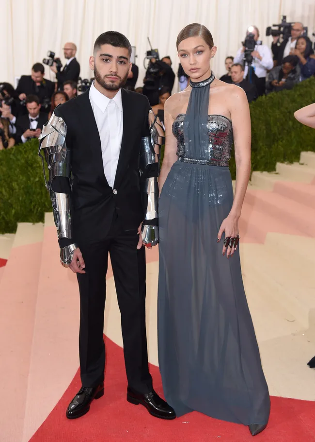 A couple poses on the red carpet, the man in a suit with metallic sleeves and the woman in a silver sequined halter gown.