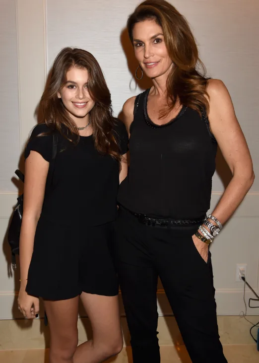 Two women posing together, both wearing black outfits, smiling at the camera indoors.