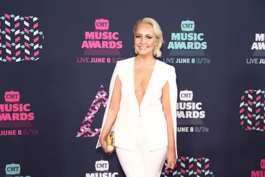 A woman in a white outfit stands smiling on the CMT Music Awards red carpet.