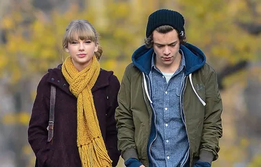 Two people walking outdoors, dressed in winter clothing with a yellow scarf and a beanie, amidst a blurred fall background.