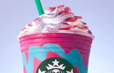 Starbucks Unicorn Frappuccino with whipped cream, colorful topping, and green straw against a light background.
