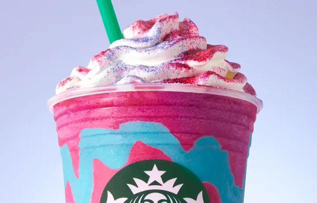 Starbucks Unicorn Frappuccino with whipped cream, colorful topping, and green straw against a light background.
