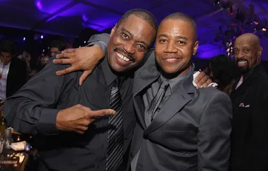 Two men in suits smiling and posing for a photo at an event with a purple-lit background.