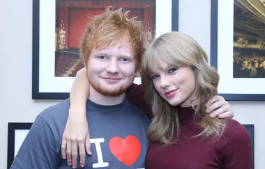Two people posing closely with arms around each other, in front of framed artwork.
