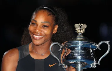 A woman smiling while holding a silver tennis trophy with engraved text.