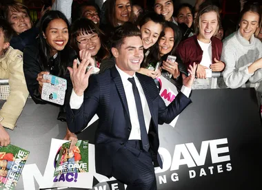 A person in a suit poses with smiling fans at a "Mike and Dave Need Wedding Dates" event.