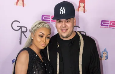 Two people posing together on a red carpet in front of a branded background.