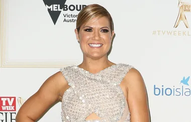 Person smiling in a sparkly dress at an event with logos in the background.