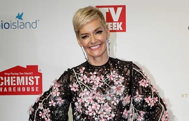 Woman in floral dress smiling on red carpet in front of TV Week backdrop.