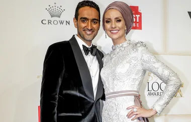 Man in black tuxedo with woman in white gown and headscarf, smiling at the Logie Awards red carpet backdrop.